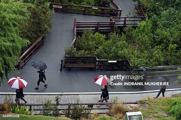 Pedestrians hold umbrellas to shield themselves from rain caused by Tropical Cyclone Marcia as they walk through a park in Brisbane on February 21,...