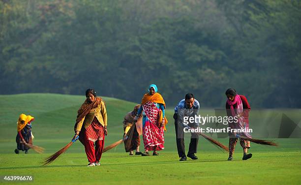 Workers wearing traditional indian dress sweep the fairway prior to the third round of the Hero India Open Golf at Delhi Golf Club on February 21,...