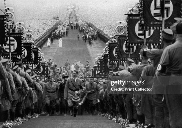Adolf Hitler at the Bückeberg Harvest Festival, Germany, 1 October 1934. Hitler climbing steps between ranks of Nazis holding swastika banners. Huge...