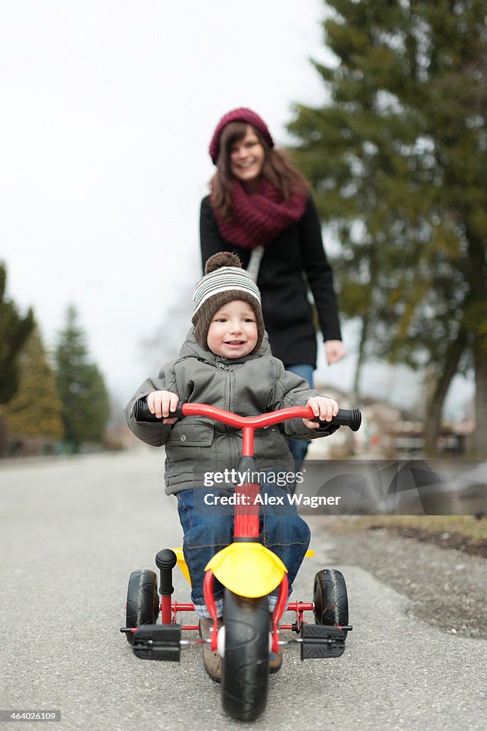 Boy on tricycle with mother in background