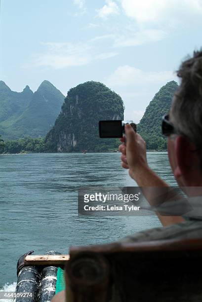Tourist photographs the spectacular scenery along the Li River while floating on a bamboo raft in Yangshuo. Speckled with karst mountains and the...