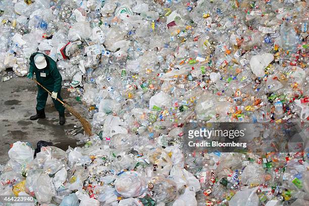 Worker uses a broom to arrange unsorted recyclable materials including plastic bottles made of polyethylene terephthalate , steel and aluminum cans...