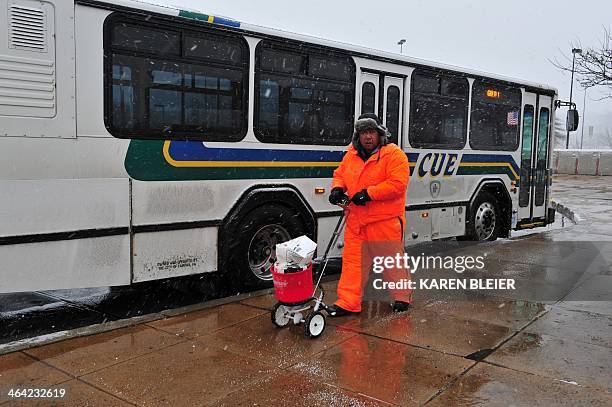 Worker spreads ice melt to sidewalks at the Vienna Metro station during a snowfall January 21, 2014 in Vienna, Virginia. The Washington, DC area and...