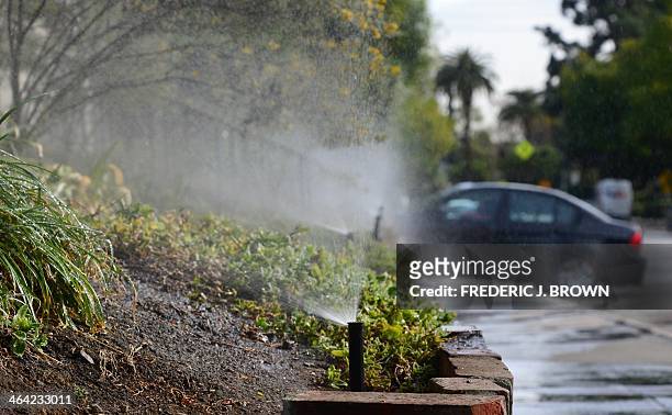 Vehicle enters a driveway at the end of a row of sprinklers watering plants and foliage in front of an apartment complex in South Pasadena,...