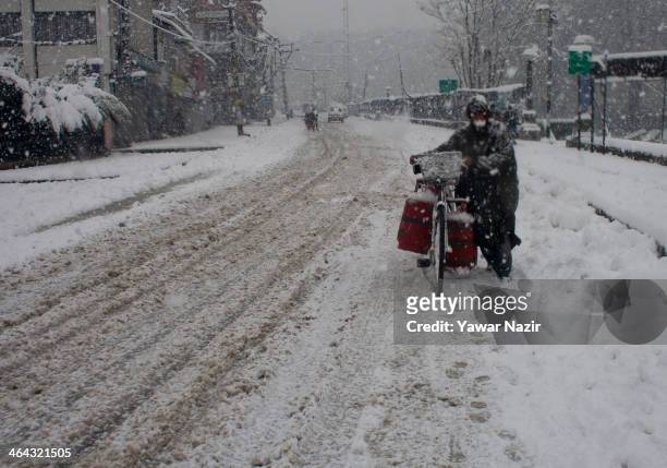Kashmiri man carries gas cylinders on his bicycle as he walks during snowfall on January 22, 2014 in Srinagar, Indian Administered Kashmir, India....