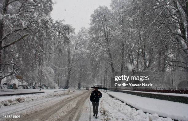 Man holds an umbrella as he walks on a road during snowfall on January 22, 2014 in Srinagar, Indian Administered Kashmir, India. Several parts of the...