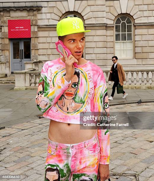 Patrick Chuch, artist wearing a crop top and trousers printed with a self portrait while holding a Moschino hand mirror shaped Iphone holder during...