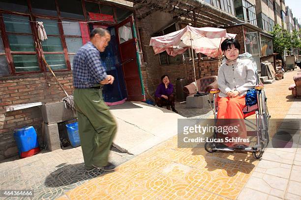 May 07: A neighbor walks pass Li Yan sitting in her wheel-chair in a residence on May 7, 2007 in Yinchuan, Ningxia Province, China. 28-year-old Li...