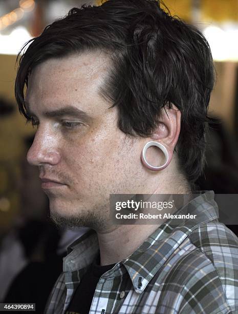 Young man wears a type of extreme earrings known as 'flesh tunnels,' which are metal discs inserted into ear piercing that stretch out the holes in...