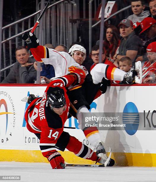 Lance Bouma of the Calgary Flames is hit by Adam Henrique of the New Jersey Devils during the first period at the Prudential Center on February 25,...