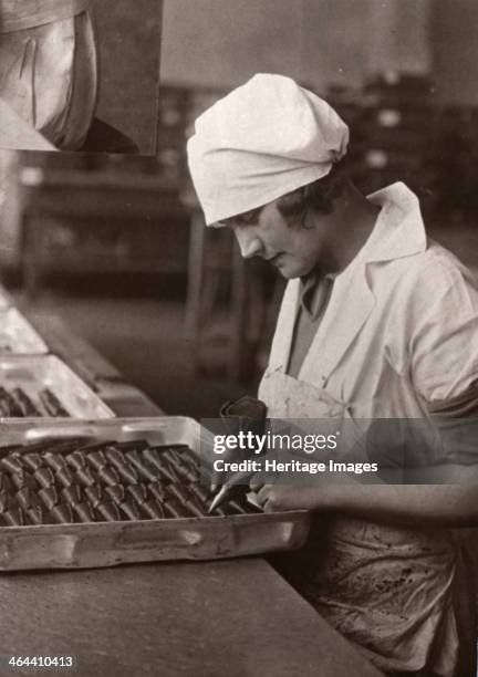 Woman uses a piping bag to decorate chocolates in a tray, Rowntree factory, York, Yorkshire, 1932.