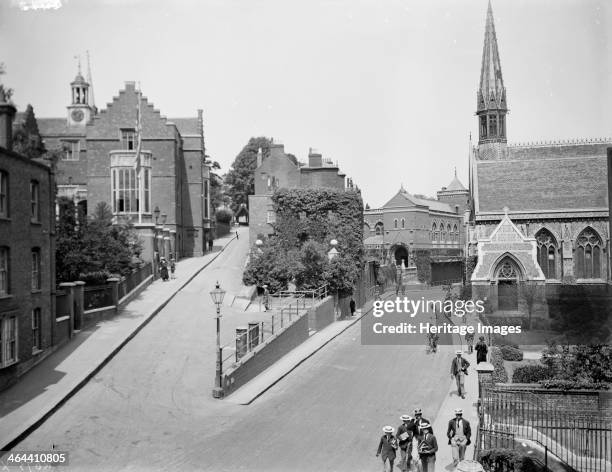 Harrow School, Harrow on the Hill, London. Pupils in school uniform can be seen carrying books along the street past the church. Former pupils...