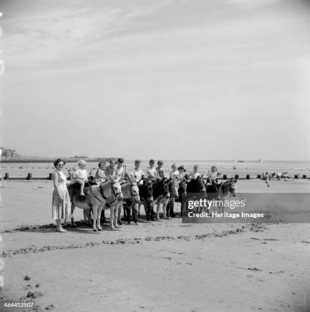 Donkey rides on the beach, Bridlington, East Riding of Yorkshire, 1950s. Eleven children enjoy a donkey ride during the summer holidays. A mother in...