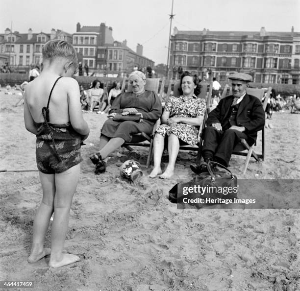 Child photographs his mother and grandparents on the beach, Blackpool, c1946-c1955. The Promenade provides a backdrop.