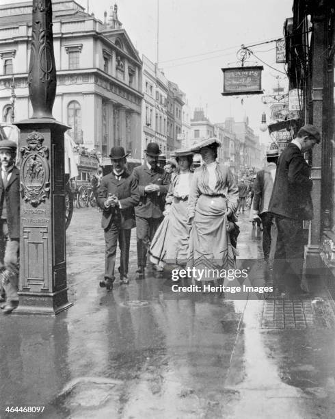 Two suffragettes walking along a pavement, London, 1900s. Holding the hems of their skirts off the wet pavement.