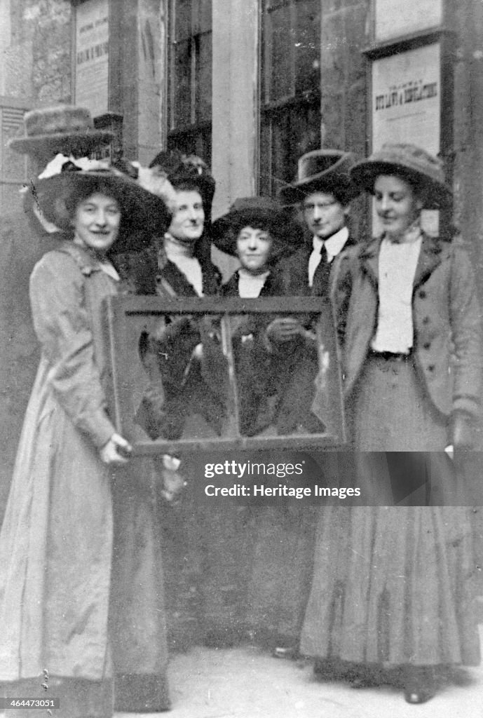 Five suffragettes holding a broken window in its frame, 1912.
