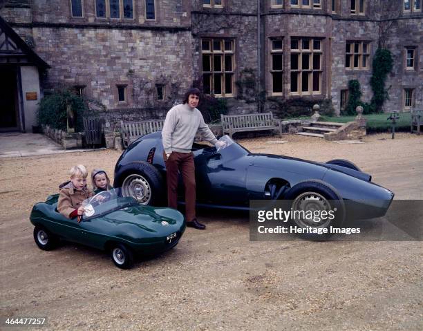 Jackie Stewart posing with a 1957 BRM. Beside him his two children sit in a miniature racing car. He began his Formula 1 career in 1965, winning the...