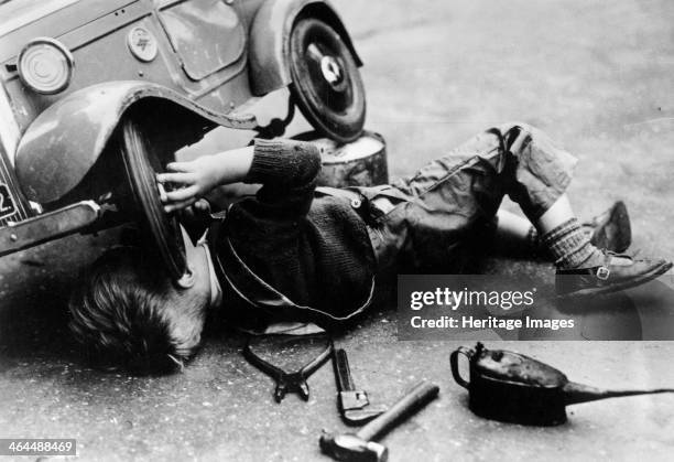 Michael Ware repairing his pedal car. Tools are lying on the ground beside him. Michael Ware became the director of the National Motor Museum Trust.