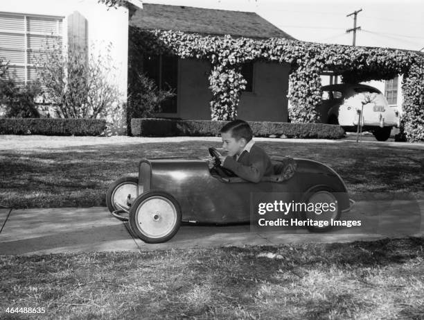 Boy in a pedal car. Driving his pedal car on the pavement outside his house.