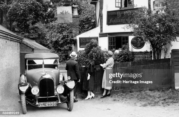 Bentley 3 litre, 1920s. Three people stand beside their car outside what appears to be a pub.