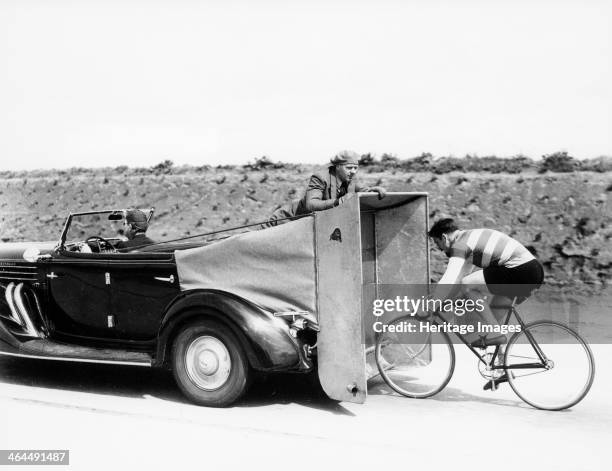 Cyclist training behind an Auburn car, c1935. The cyclist rides along behind an improvised windbreak attached to the car.