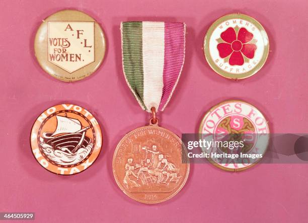 Collection of suffragette badges, 1900s. The medal in the centre depicts a suffragette being force fed in prison. She is being held down and a tube...