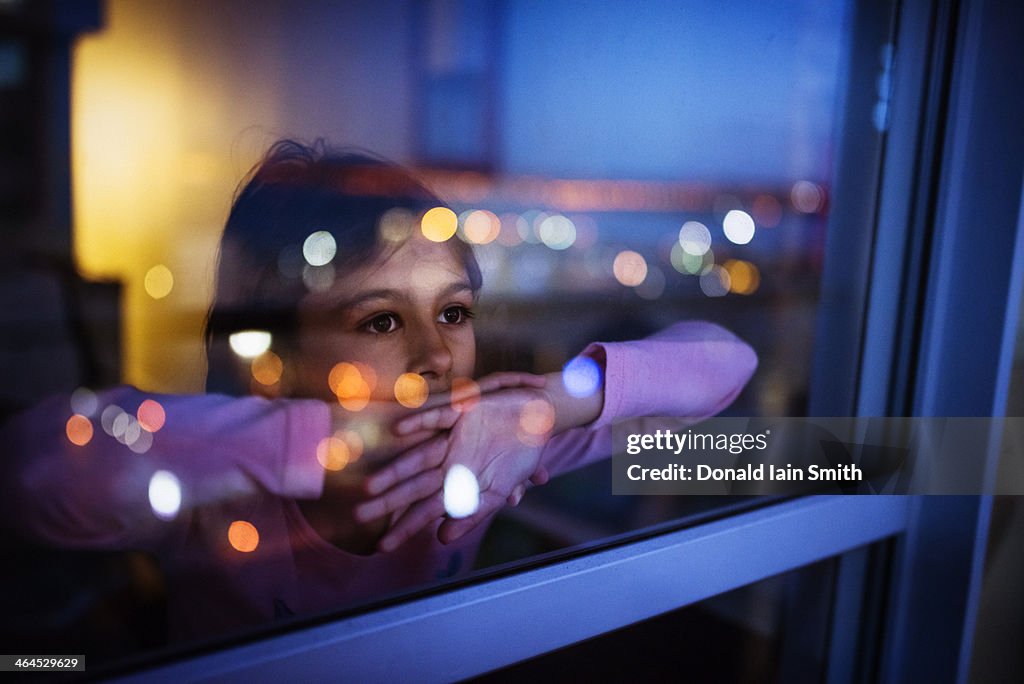 Girl at window with reflected city lights