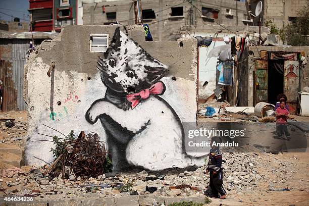 Children are seen near to a graffiti on a wall of a building drawn by British artist Banksy in Beit Hanoun, Gaza on February 27, 2015. Famous British...