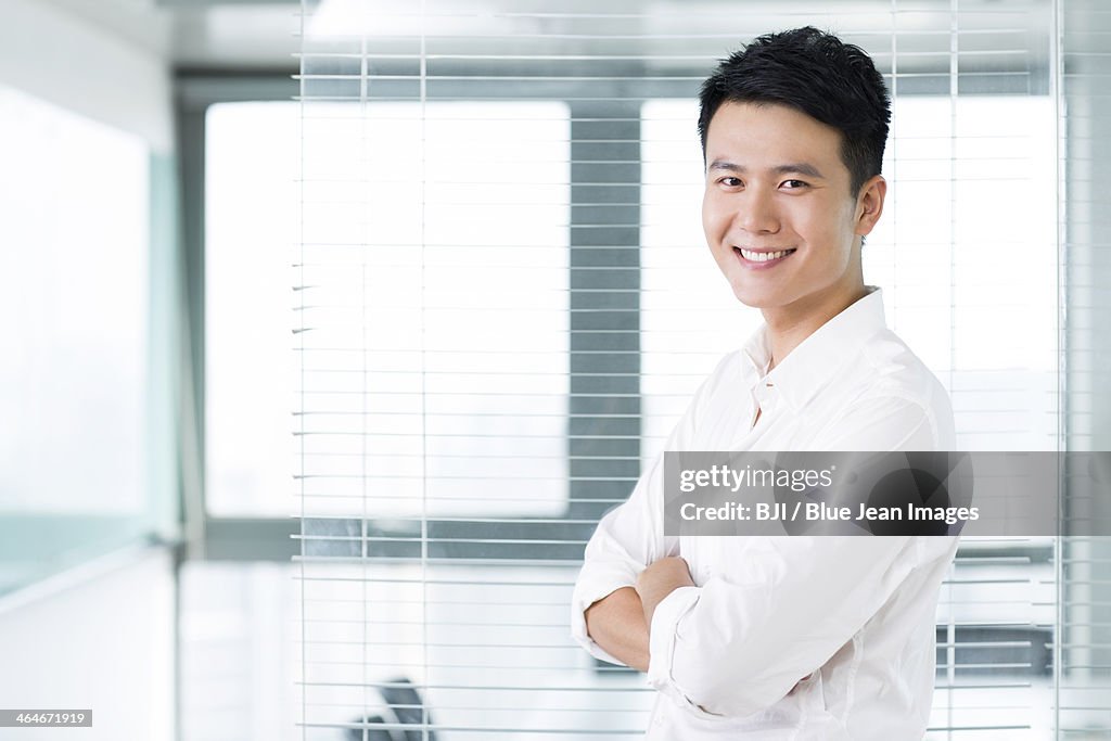 Portrait of young man arms crossed in office