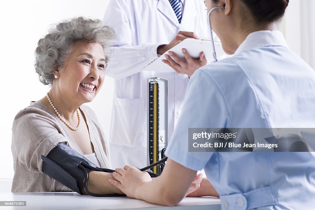 Nurse taking senior woman's blood pressure