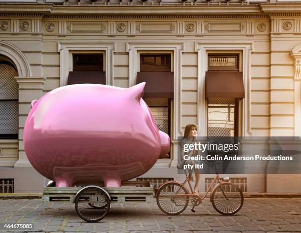 caucasian girl pulling piggy bank on bicycle cart - spardose stock-fotos und bilder