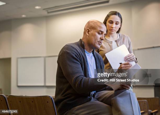 professor and student reviewing essay in lecture hall - male professor with students stock pictures, royalty-free photos & images