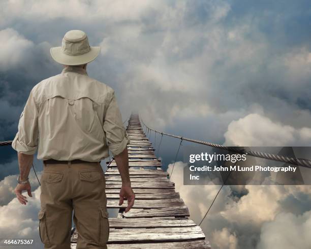 caucasian explorer examining wooden rope bridge in clouds - touwbrug stockfoto's en -beelden