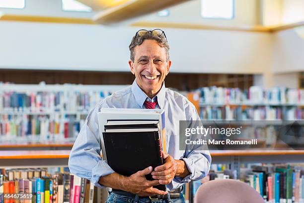 senior man holding books in library - librarian stock-fotos und bilder