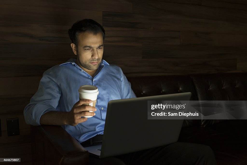 Businessman using laptop on sofa at night