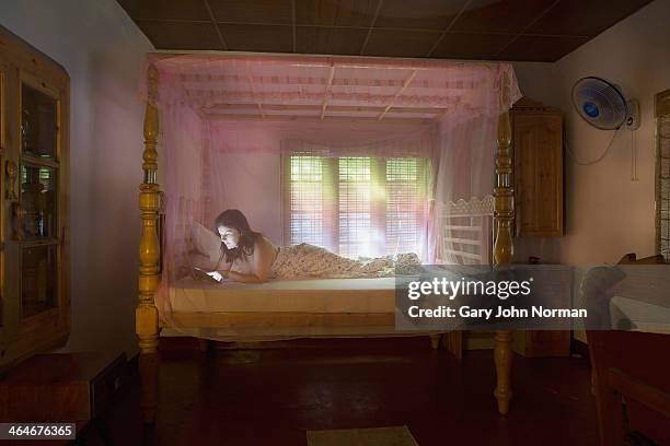 woman with tablet computer in bed under mosquito net - mosquito netting stock pictures, royalty-free photos & images