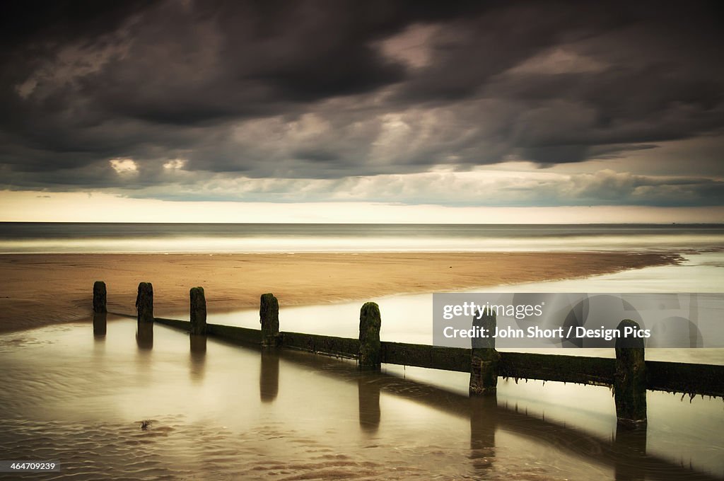 A Fence Submerged In The Water At The Coast With Storm Clouds Overhead