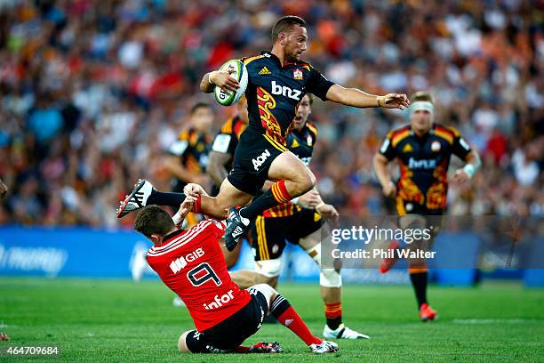 Aaron Cruden of the Chiefs leaps over the tackle of Mitchell Drummond of the Crusaders during the round three Super Rugby match between the Chiefs...