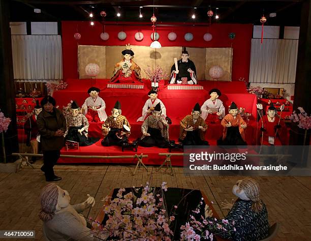 Woman walks beside the illustration showing human size scarecrows as hina doll dressed in traditional Japanese Hinamatsuri costumes are on display...