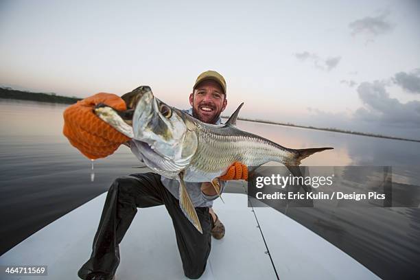 a man proudly holds a large fresh caught fish on the stern of a boat - catch of fish stock pictures, royalty-free photos & images