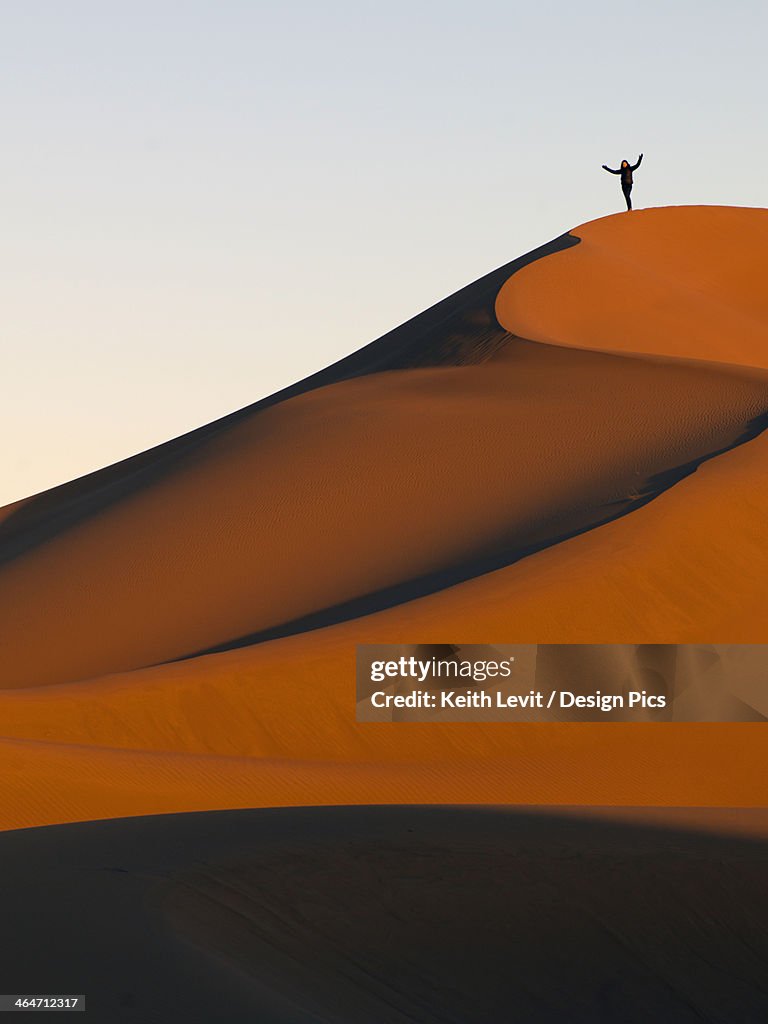 A Person Stands On A Top Ridge Of A Sand Slope