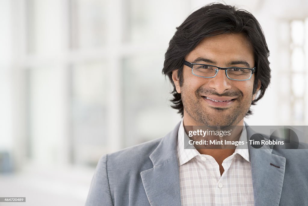 A business environment, a light airy city office. Business people. A man in a light jacket wearing glasses.