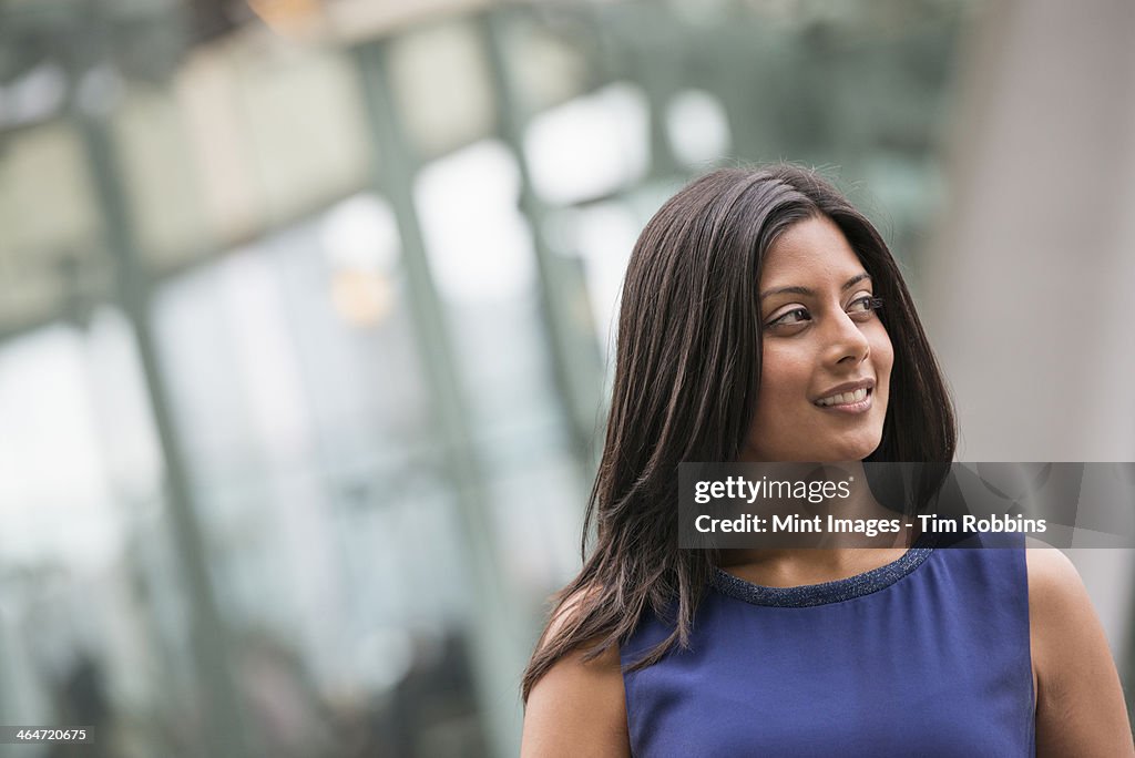 Business people out and about in the city. A woman with long black hair wearing a blue dress.