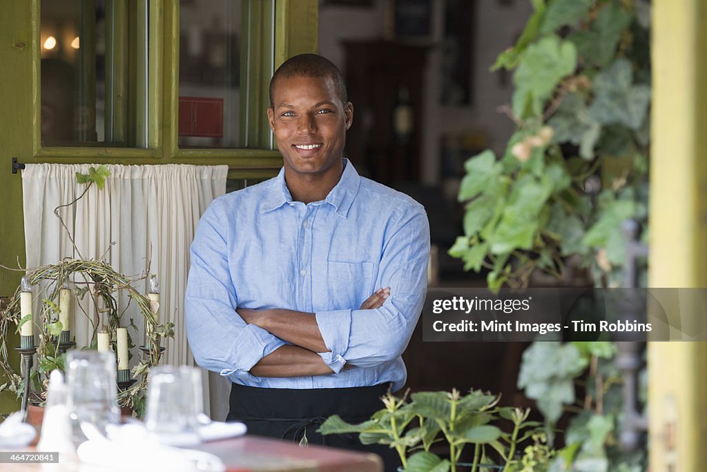 A man standing by the open window of a cafe or bistro, looking out with arms folded. 