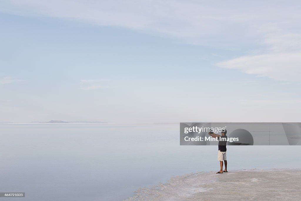 A man standing at edge of the flooded Bonneville Salt Flats at dusk, taking a photograph with a tablet device, near Wendover.