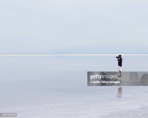 a man standing on the edge of the flooded bonneville salt flats, taking a photograph at dusk. - bonneville salt flats 個照片及圖片檔