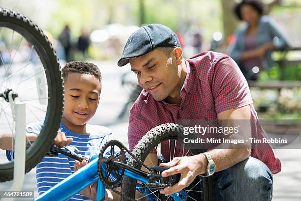 a family in the park on a sunny day. a father and son repairing a bicycle. - repairing bike stock pictures, royalty-free photos & images