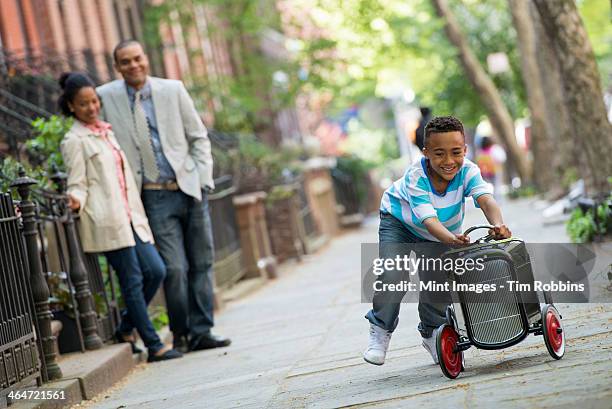 a young boy playing with a old fashioned toy car on wheels on a city street. a couple looking on. - new york summer press day stockfoto's en -beelden