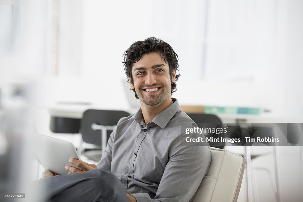 An office in the city. Business. A man seated smiling and holding a digital tablet.