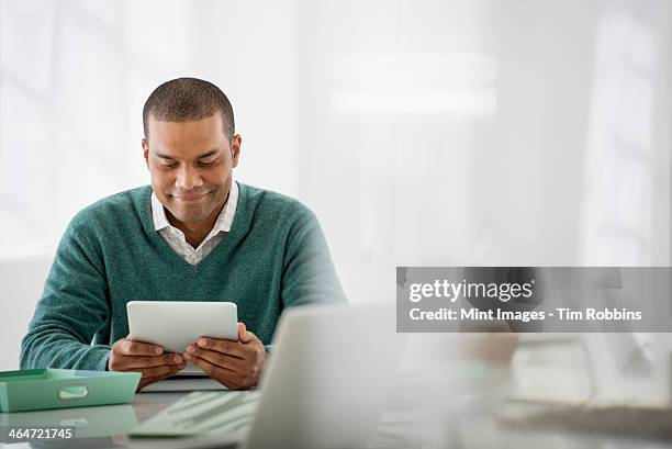 business. a light airy office environment. a man sitting holding a digital tablet. - grünes hemd stock-fotos und bilder